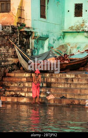 India, Varanasi - Uttar Pradesh stato, 31 luglio 2013. All'alba, un uomo lava i vestiti sul fiume Gange, mentre un barcaiolo si appoggia sulla barca. Foto Stock