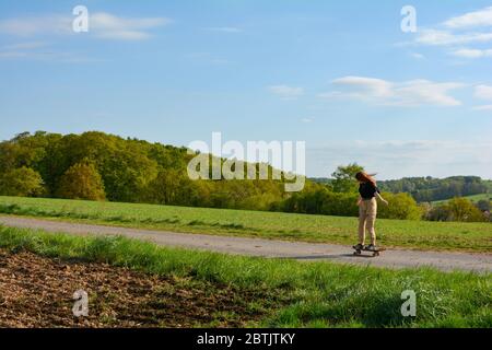 Una ragazza guida uno skateboard su una strada di campagna in natura verde Foto Stock