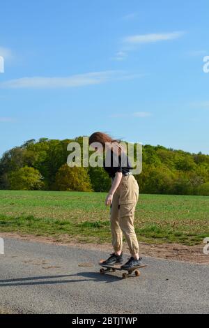 Una giovane donna guida uno skateboard su una strada di campagna in natura verde Foto Stock