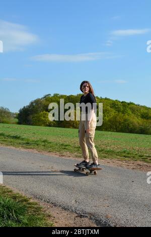 Una ragazza guida uno skateboard su una strada di campagna in natura verde Foto Stock