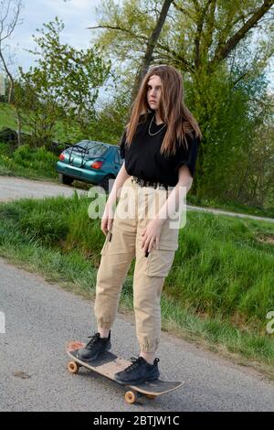 La giovane ragazza si muove su una strada di campagna in natura verde, con un'auto sullo sfondo Foto Stock