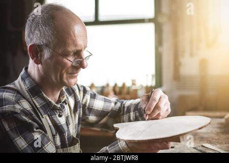 Falegname maturo che segna un pezzo di legno con una matita Foto Stock