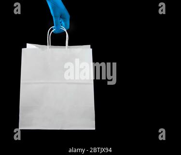 Una persona che indossa guanti di lattice protettivi che tiene una borsa di carta per la spesa Foto Stock