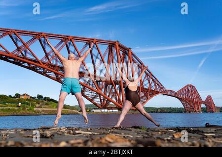 North Queensferry, Scozia, Regno Unito. 26 maggio 2020. Kenny McAlpine e Jenny Waring dal gruppo di bagnanti Fife Wild, si sforza del caldo sole e si può fare una fuga in esercizio dal Lockdown Covid-19 e si salta nel Firth of Forth a North Queensferry con il Forth Bridge come sfondo spettacolare. Iain Masterton/Alamy Live News Foto Stock