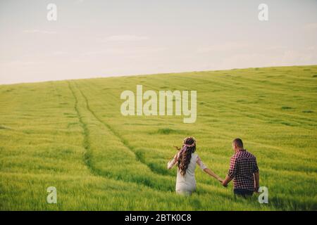 attesa bambino. Genitorialità. La giovane donna incinta e il marito sono felici di tenere le mani, andando all'aperto nel campo di sfondo verde erba. S Foto Stock