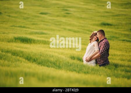 attesa bambino. Genitorialità. La giovane donna incinta e il marito sono felici di tenere le mani, andando all'aperto nel campo di sfondo verde erba. S Foto Stock