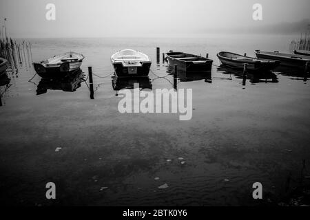 piccole barche a remi si trovano sulla riva di un lago nella nebbia Foto Stock