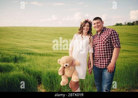 attesa bambino. Genitorialità. La giovane donna incinta e il marito sono felici di tenere le mani, andando all'aperto nel campo di sfondo verde erba. S Foto Stock