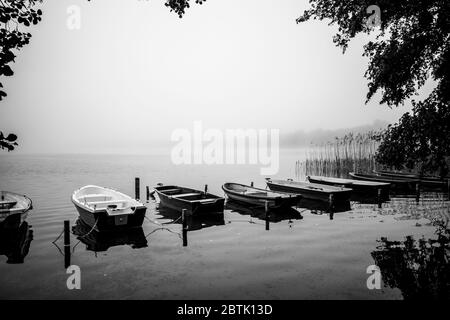 piccole barche a remi si trovano sulla riva di un lago nella nebbia Foto Stock