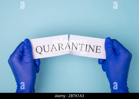Concetto di quarantena finale. In alto sopra la vista dall'alto foto delle mani in guanti che si strappano la parola di quarantena isolata su sfondo blu Foto Stock