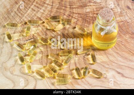 La luce solare brillante splende attraverso una bottiglia di olio vegetale e capsule oblunghe trasparenti con olio di pesce su sfondo di legno. Omega-3-polyu essenziale Foto Stock