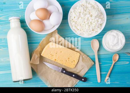 Latte fresco, formaggio di cottage, panna acida e formaggio su carta, nonché uova in una ciotola giacciono su un tavolo di legno blu. Naturale e sano, ricco di calcio Foto Stock
