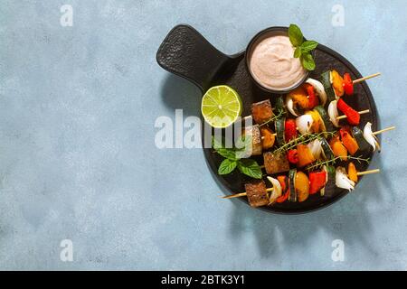 kebab vegani pronti di verdure e tofu affumicato con salsa di anacardi e paprika affumicata su sfondo blu Foto Stock