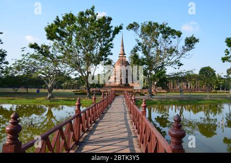 Un ponte rosso conduce a Wat Sra Sri, un bellissimo tempio nel parco storico di Sukhothai Foto Stock