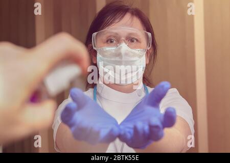 L'operatore sanitario in maschera medica protettiva facciale, guanti, occhiali di sicurezza e con stetoscopio utilizza igienizzatore per proteggere le mani durante la corona Foto Stock