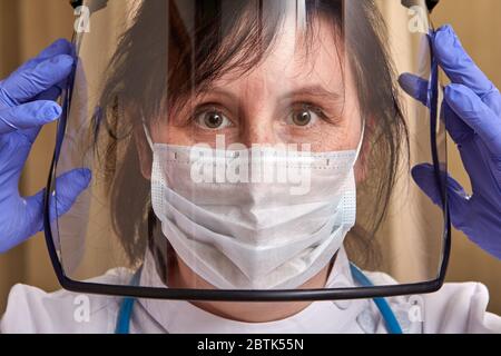 Grave donna caucasica medico in uniforme protettiva con maschera chirurgica e guanti come protezione da infezione da coronavirus covid-19. Un'assistenza sanitaria Foto Stock