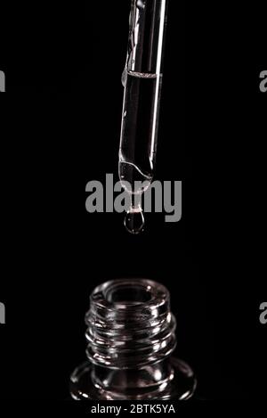 Primo piano su una pipetta con una goccia di liquido che cade in una fiala Foto Stock