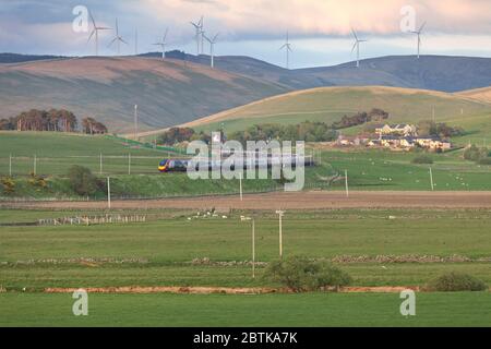 Treni Virgin Alstom Pendolino treno sulla linea principale della costa occidentale nella valle di Clyde, Scozia, con un parco eolico che mostra il trasporto verde Foto Stock