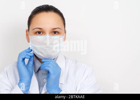 ritratto facciale di una dottoressa in abito da vestizione, maschera respiratoria e guanti, guardando la fotocamera. Su sfondo bianco. Con posizione per copia sp Foto Stock