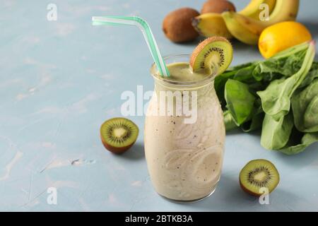 Smoothie kiwi, banana, spinaci e limone sano in vaso di vetro su sfondo azzurro con ingredienti freschi, dieta e controllo della perdita di peso Foto Stock