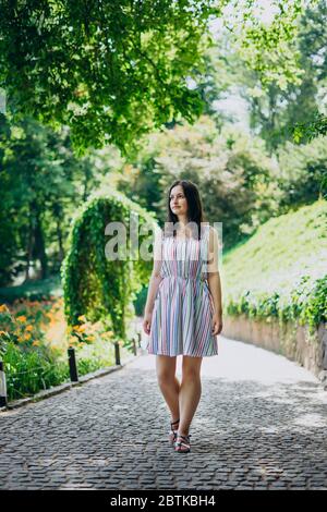 Sofia Park, Uman. La ragazza cammina lungo i vicoli del parco in una giornata di sole. Bruna ragazza in un vestito bianco cammina in un bellissimo parco paesaggistico. Percorso Foto Stock