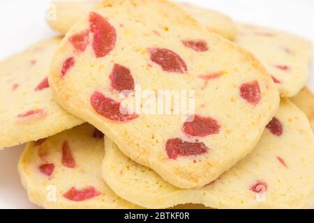 Vista ravvicinata di una pila di biscotti tradizionali appena fatti a fette croccanti e dolci, biscotti dorati fatti in casa con pezzi di ciliegia rossa Foto Stock