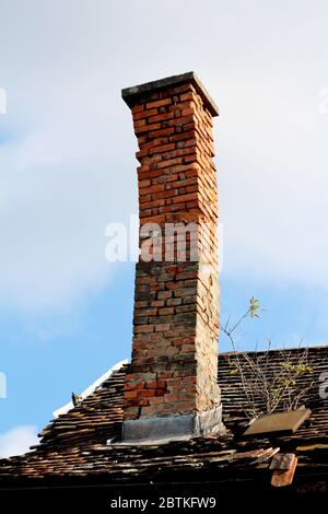 Camino inclinato crooked vecchio fatto di mattoni rossi dilapidati spaccati con tappo in cemento sulla parte superiore costruito sul tetto di casa suburbana abbandonata famiglia Foto Stock