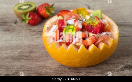 macedonia di frutta in una pentola di pompelmo. frutta su fondo di legno. Foto Stock