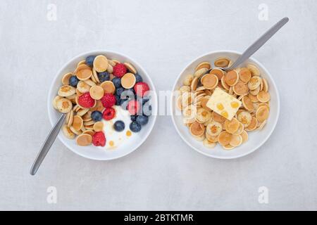 Ciotola di frittelle di cereali con mirtilli lamponi yogurt e sciroppo d'acero e una ciotola con cereali pancake burro e sciroppo Foto Stock