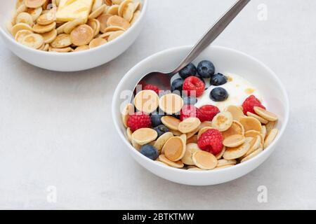 Ciotola di frittelle di cereali con mirtilli lamponi yogurt e sciroppo d'acero e una ciotola con cereali pancake burro e sciroppo Foto Stock