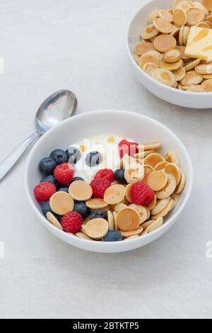 Ciotola di frittelle di cereali con mirtilli lamponi yogurt e sciroppo d'acero e una ciotola con cereali pancake burro e sciroppo Foto Stock