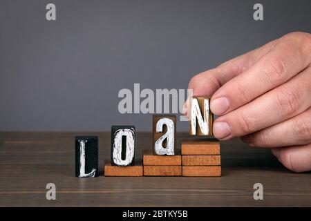 PRESTITO. Concetto di transazione, approvazione, debito e passività. Lettere alfabetiche in legno sui gradini. Sfondo grigio Foto Stock