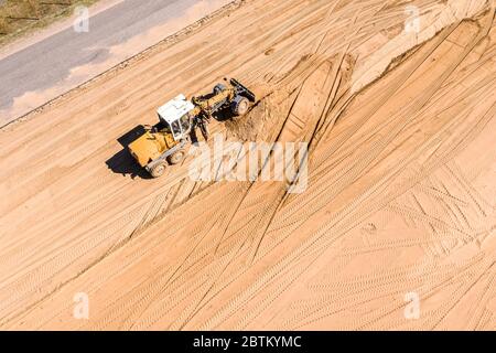 cantiere stradale con macchine pesanti. livellatore giallo livella il terreno per lavori edili. vista aerea Foto Stock