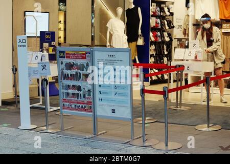 Un GU a Ginza durante l'epidemia di coronavirus, un avviso chiede ai clienti di indossare maschere facciali e un membro del personale attende di prendere le temperature dei clienti. Foto Stock
