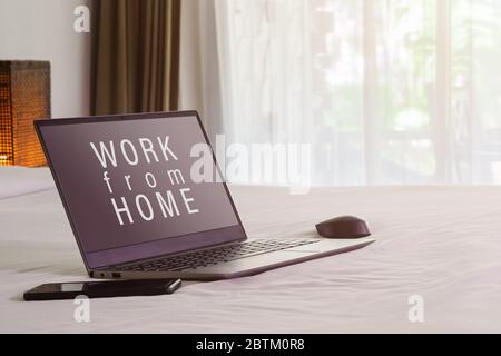 Concetto di lavoro da casa. Il computer portatile e il computer al mattino su un letto bianco. Lavorare a casa per IL CORONAVIRUS o COVID-19 prevenzione concetto in letto Foto Stock