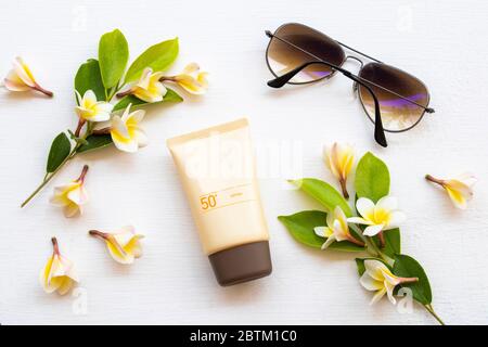 crema solare spf50 cosmetici cura della salute per la pelle viso, occhiali da sole e fiori gialli frangipani di stile di vita donna relax in estate stagione Foto Stock