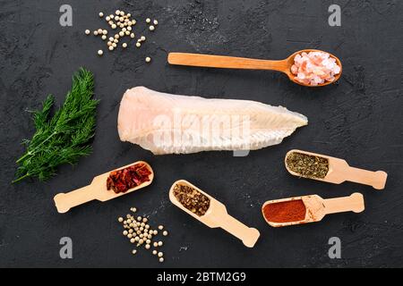 Filetto di nasello crudo poco profondo con spezie ed erbe su fondo nero Foto Stock