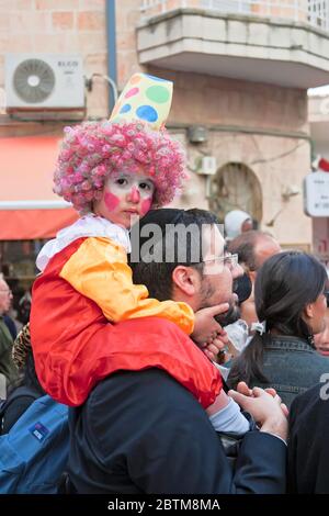 Carnevale di Purim a Gerusalemme. Persone non identificate guardano lo spettacolo. Sulle spalle dell'uomo siede un bambino non identificato vestito come un clown. Purim è cele Foto Stock