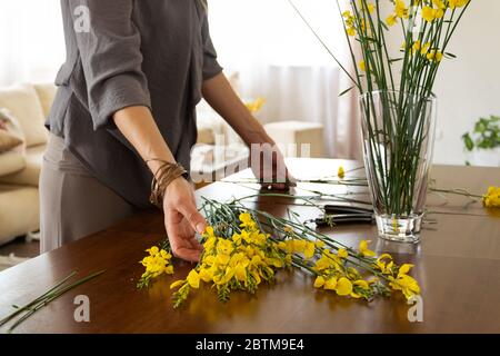 Vista di raccolto di donna che dispone gorse di fiore giallo a casa Foto Stock
