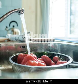 Verdure fresche sotto un flusso d'acqua in un colapasta nel lavandino, in cucina, sullo sfondo di un asciugamano e di un bollitore. Foto Stock