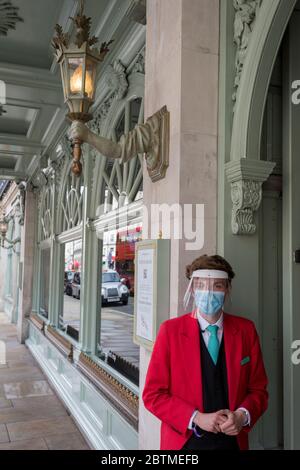 Durante il blocco della pandemia di Coronavirus nel Regno Unito e nelle 24 ore in cui si sono verificati altri 255 decessi, portando i decessi ufficiali del covid a 37,048, un dipendente Fortnum & Mason indossando una maschera e uno scudo facciale si trova fuori dal famoso grande magazzino di Piccadilly, In preparazione della riapertura della loro Food Hall il 15 giugno, secondo le linee guida governative, il 26 maggio 2020, a Londra, Inghilterra. Foto Stock