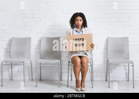 Disperato signora che tiene il segno ho BISOGNO DI LAVORO mentre attende l'intervista di occupazione all'ufficio dell'azienda. Spazio per il testo Foto Stock