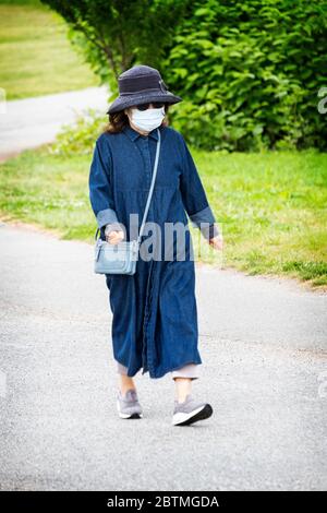 Una donna asiatica americana che cammina e indossa la sua maschera chirurgica in una fredda mattina di primavera. A Little Bay Park, Whitestone, Queens, New York. Foto Stock