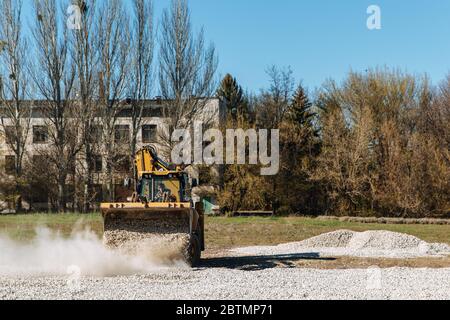 Dneprorudnoe/Ucraina - Aprile 08 2020: Un trattore versa la ghiaia dalla benna Foto Stock