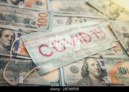 La maschera medica è su 100 dollari di fondo fatture. Concetto di dipendenza economica dalla pandemia di coronavirus COVID-19 Foto Stock