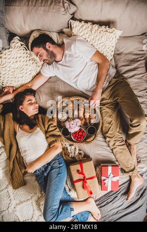 Felice coppia sorridente sdraiata a letto e dopo la colazione festiva Foto Stock