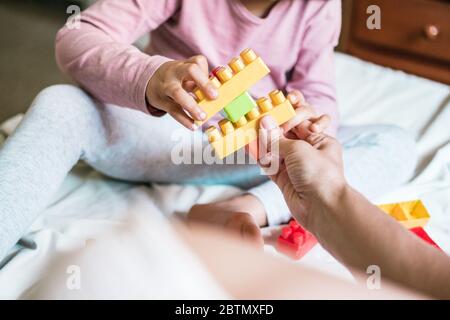 Primo piano di madre e le mani di sua figlia che giocano gioco di costruzione come si uniscono alcuni mattoncini giocattolo insieme. Sono seduti su un letto Foto Stock