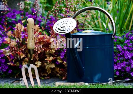 Tradizionale metallo annaffiatura lattina e attrezzi da giardino con un bel giardino stile cottage sullo sfondo Foto Stock