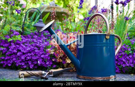 Tradizionale metallo annaffiatura lattina e attrezzi da giardino con un bel giardino stile cottage sullo sfondo Foto Stock