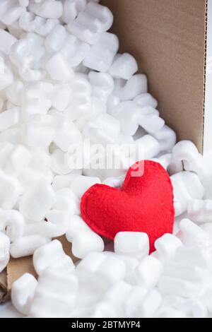 Scatola di confezionamento cuore in feltro rosso riempita con molti pellet di polistirolo bianco. Consegna attenta con amore Foto Stock